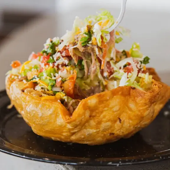 Taco salad served in a crispy tortilla bowl with lettuce, cheese, and seasoned meat