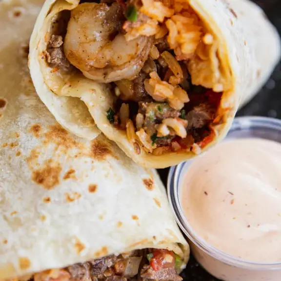 Shrimp burrito cut open with side dipping sauce